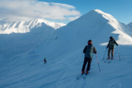 Grupa narciarzy freeride obserwuje zjeżdżającego zboczem innego narciarza