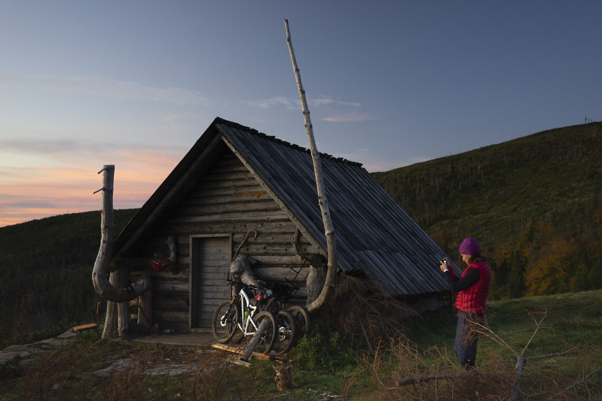 Górska chata, przed nią kilka rowerów i osoba robi zdjęcie